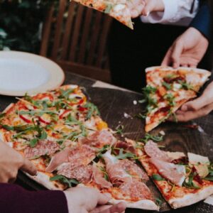 person holding pizza with cheese and green leaves